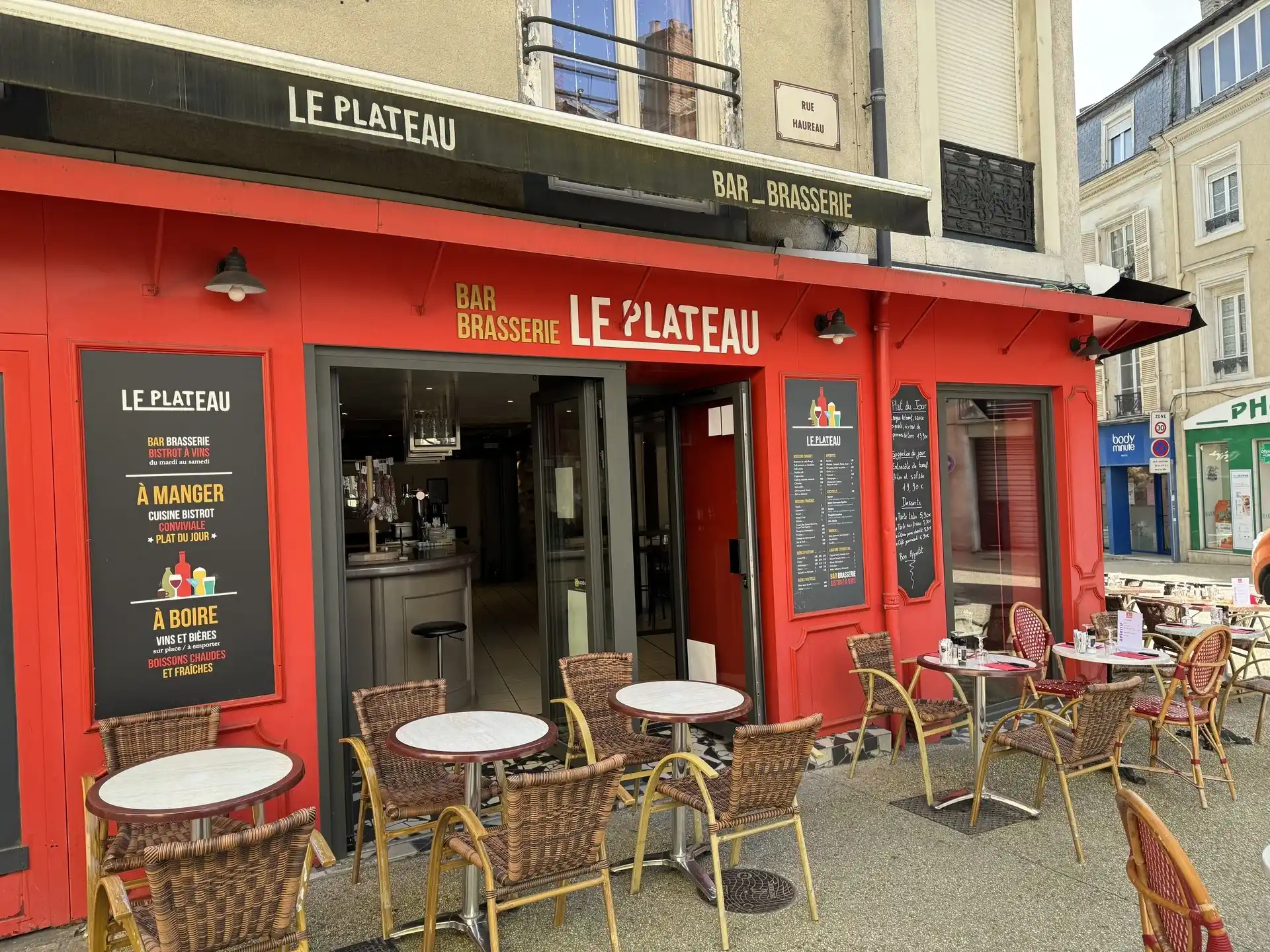 Façade rouge du Bar Brasserie Le Plateau, rue Hauréau au Mans, avec sa terrasse et ses tables en osier