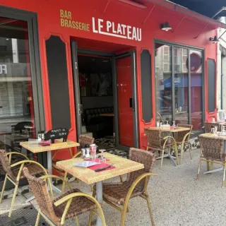 Terrasse et façade rouge du Bar Brasserie Le Plateau, tables et fauteuils en rotin